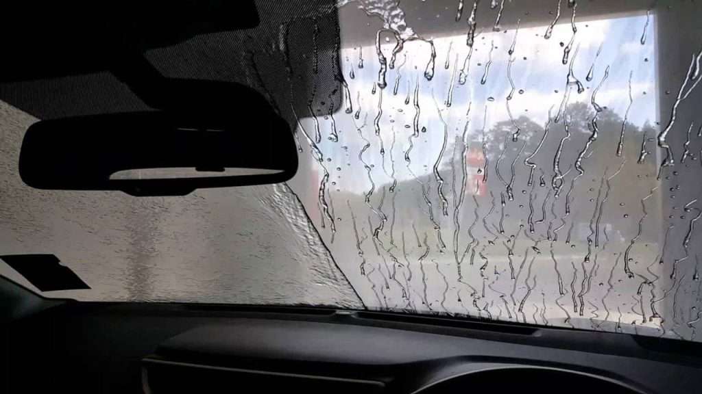 View from inside a car during a wash, windshield covered with water streaks and suds on the glass.