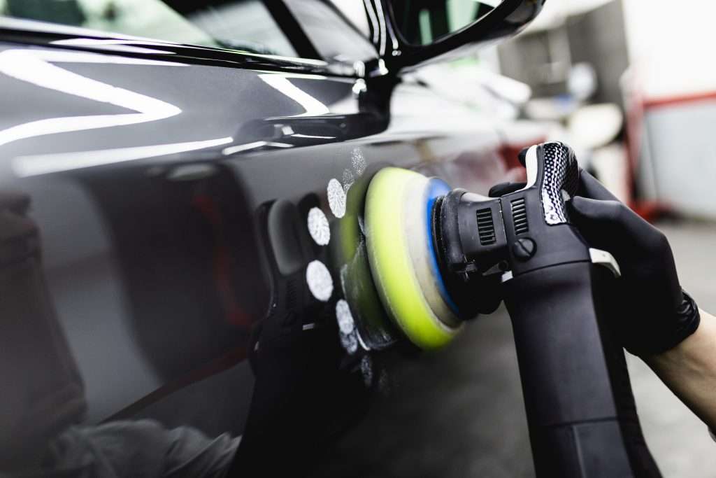 Person in gloves using a car polisher on a glossy black car surface, close-up of the polishing pad and pad motion