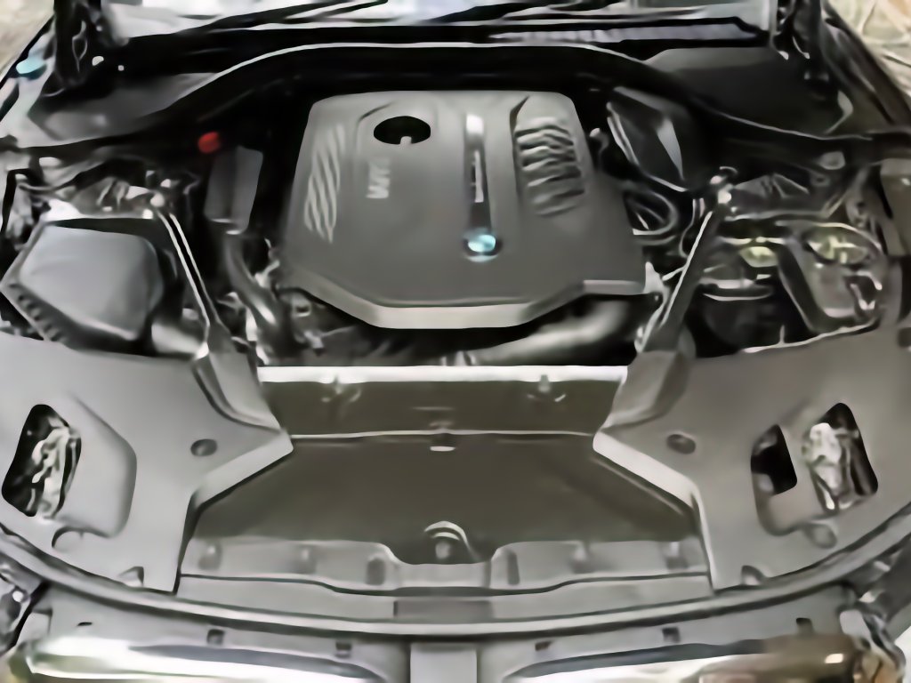View of a car engine bay with a central silver component and surrounding hoses and metal parts.